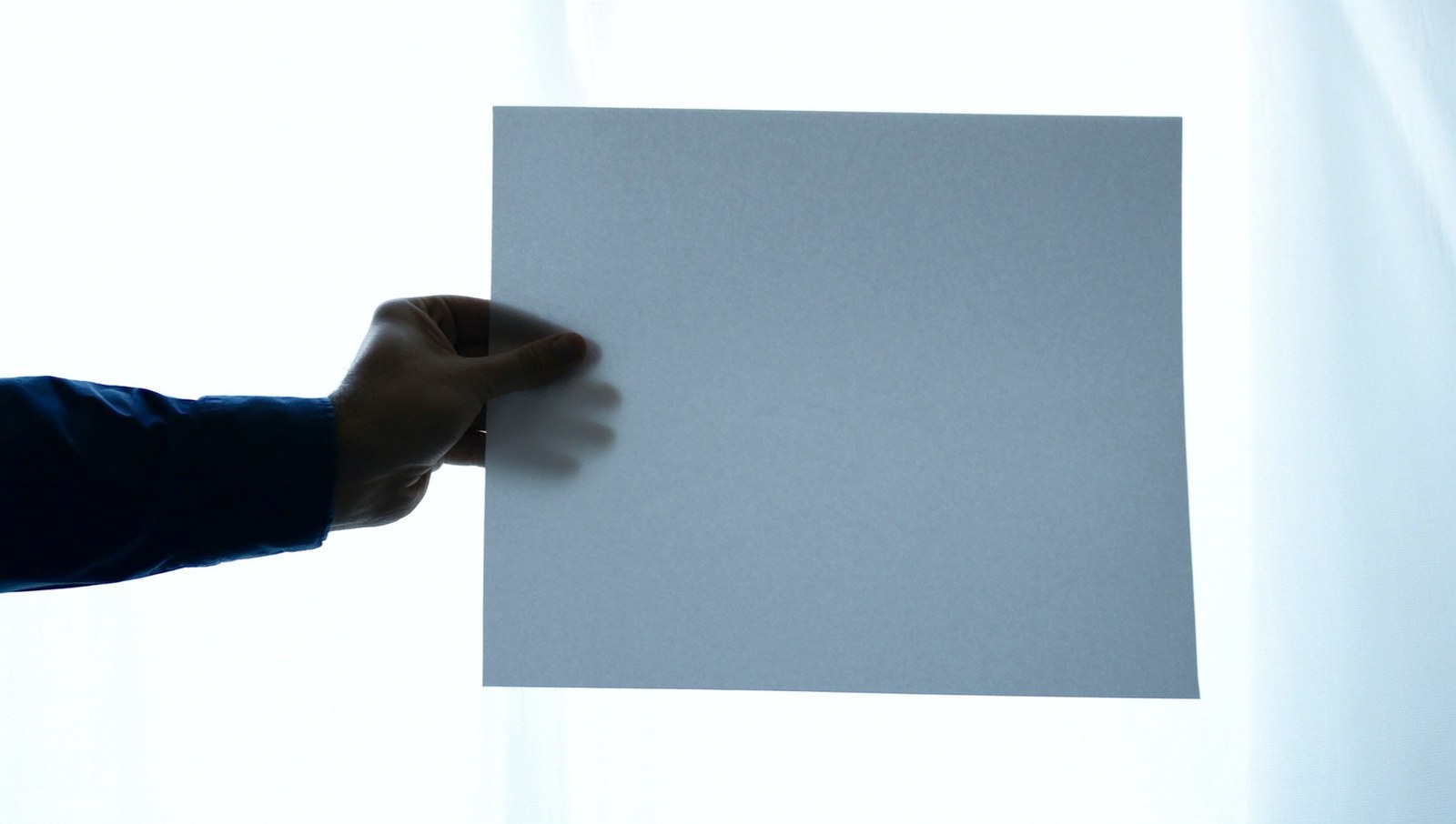 A hand holding a blank sheet of paper up to a bright window, looking for a watermark.