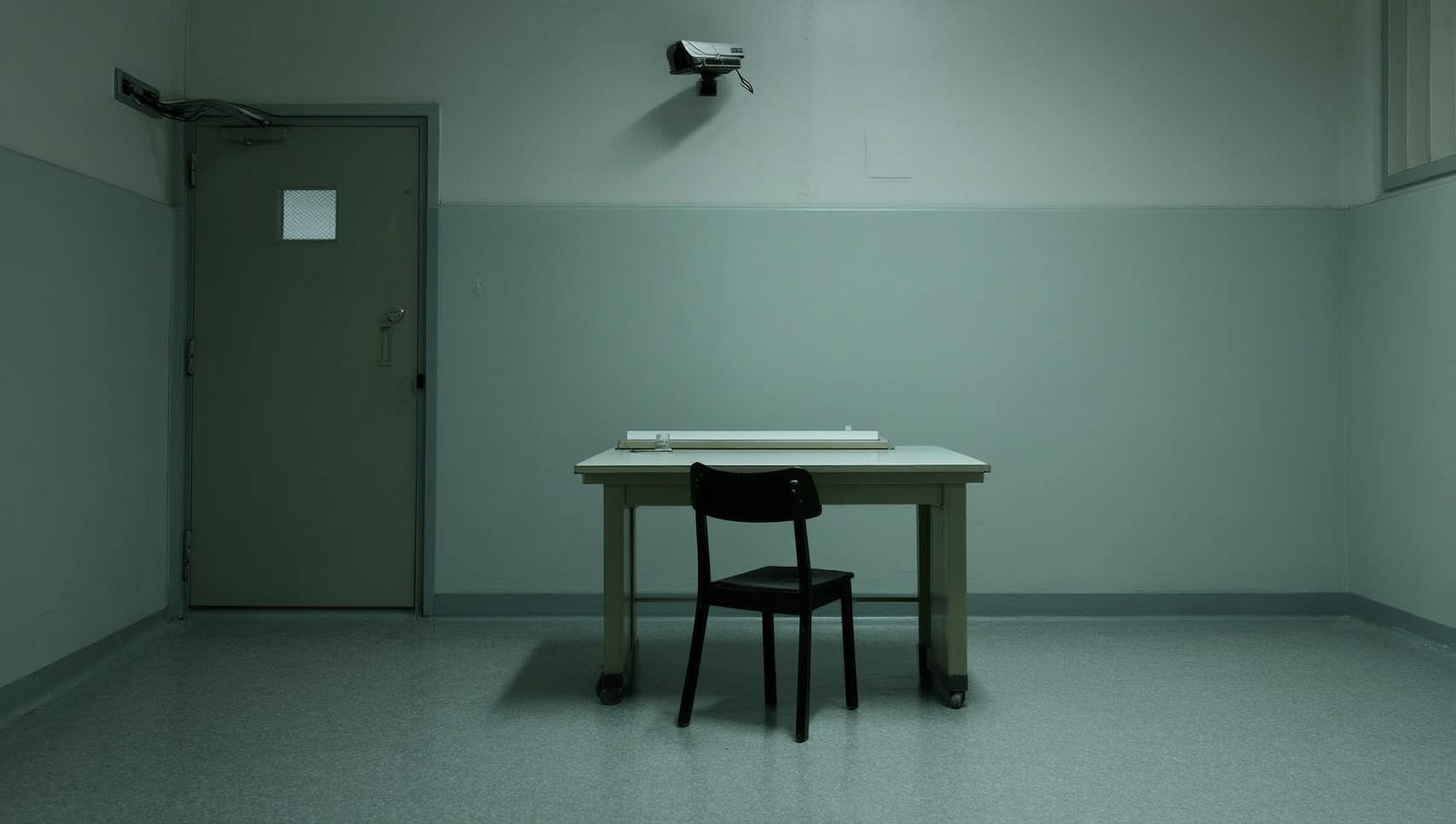 An empty proctored testing room with one chair, one desk and a camera on the wall.
